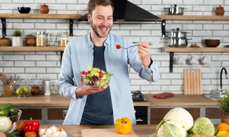 happy man standing in the kitchen eating fresh salad with fork