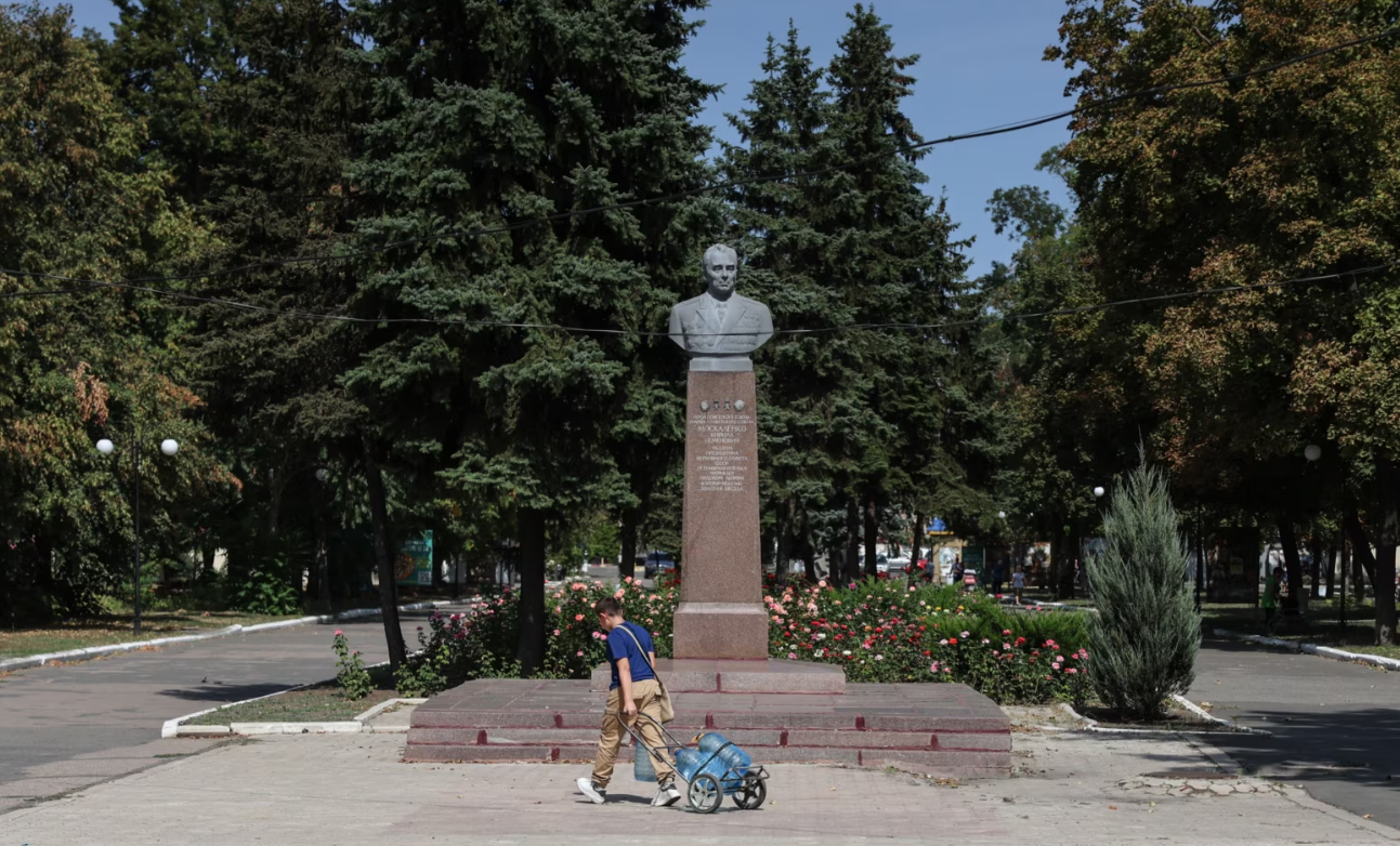 Підліток тягне «кравчучку» з водою повз пам'ятник герою Радянського Союзу Кирилу Москаленку, який народився неподалік. Покровськ, вересень 2024 року